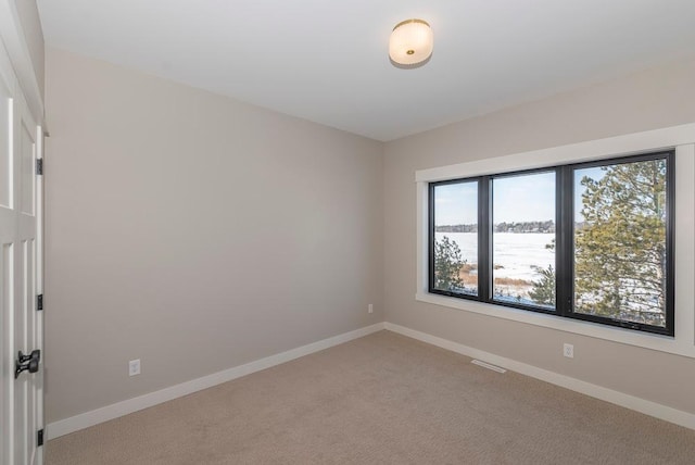 empty room featuring light colored carpet, a water view, and baseboards