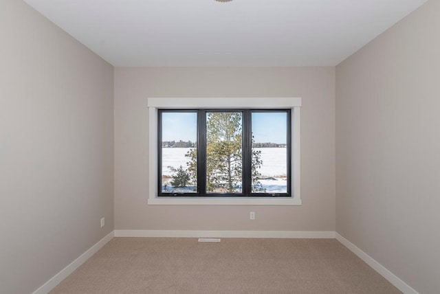 unfurnished room featuring light colored carpet, baseboards, and a water view