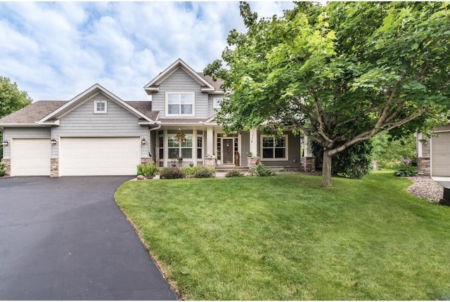 craftsman house with an attached garage, stone siding, a front yard, a porch, and aphalt driveway