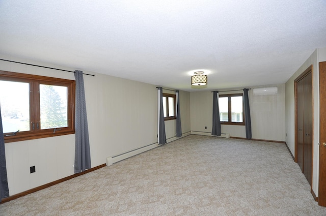 spare room with a baseboard radiator, a wall mounted AC, light colored carpet, and baseboards