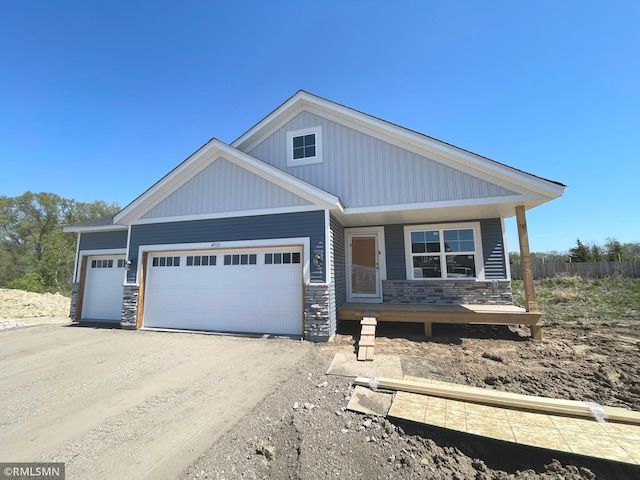 view of front of home featuring stone siding, a garage, covered porch, dirt driveway, and fence
