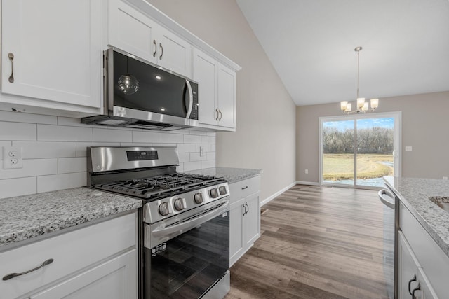 kitchen featuring stainless steel appliances, vaulted ceiling, a chandelier, light wood-type flooring, and white cabinetry