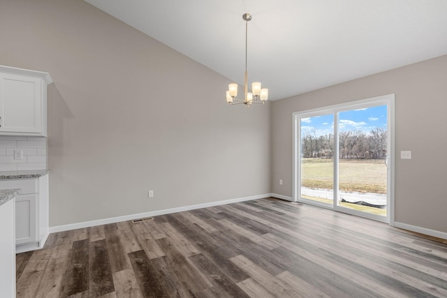 unfurnished dining area featuring lofted ceiling, a chandelier, wood finished floors, and baseboards
