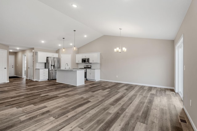 kitchen featuring appliances with stainless steel finishes, open floor plan, a chandelier, vaulted ceiling, and a kitchen island with sink