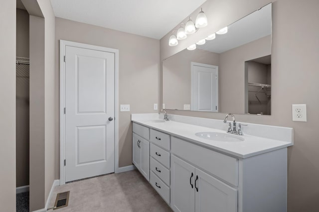 bathroom with double vanity, a walk in closet, and baseboards