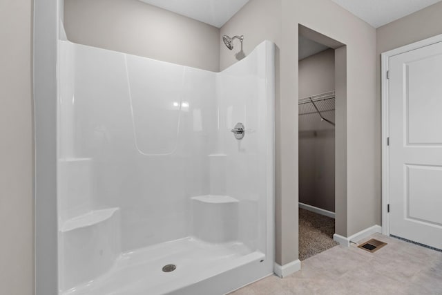 bathroom featuring a shower, a walk in closet, and baseboards