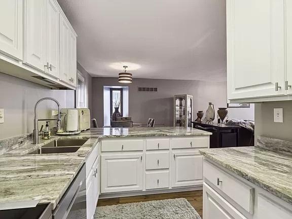 kitchen featuring a sink, stainless steel dishwasher, dark wood-type flooring, a peninsula, and white cabinetry