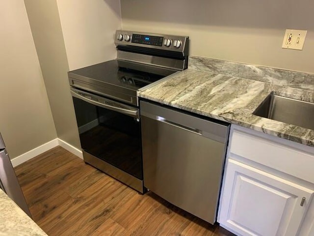 kitchen with appliances with stainless steel finishes, dark wood-type flooring, light stone counters, baseboards, and white cabinetry
