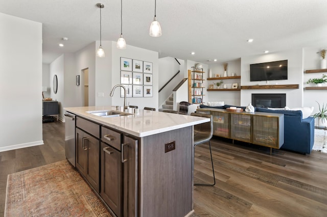 kitchen with a sink, stainless steel dishwasher, a breakfast bar area, dark wood-style floors, and a glass covered fireplace