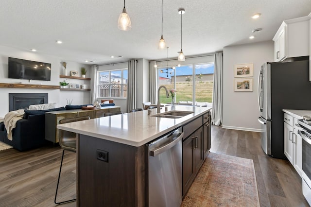 kitchen with a sink, stainless steel dishwasher, an island with sink, a kitchen breakfast bar, and dark wood-style floors