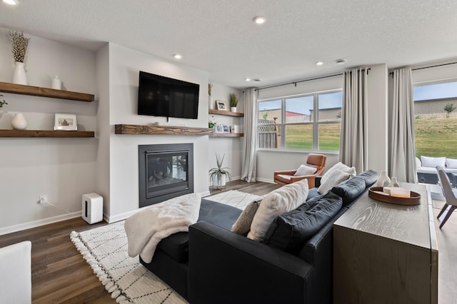living area featuring a glass covered fireplace, a textured ceiling, baseboards, wood finished floors, and recessed lighting