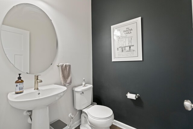 half bathroom featuring toilet, baseboards, and a sink