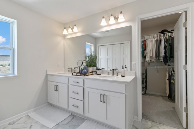 full bathroom featuring marble finish flooring, double vanity, a walk in closet, and baseboards