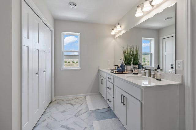 bathroom featuring plenty of natural light, marble finish floors, double vanity, and baseboards