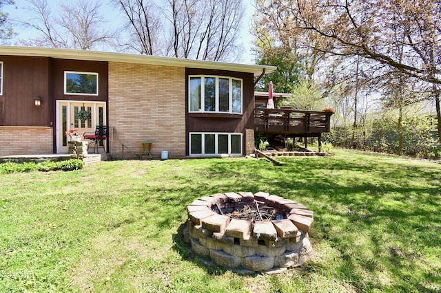 rear view of house with an outdoor fire pit, a deck, brick siding, and a lawn
