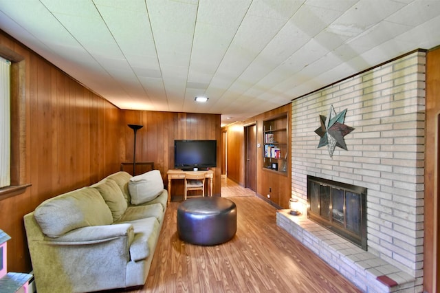 living room with wooden walls, a brick fireplace, wood finished floors, and built in shelves