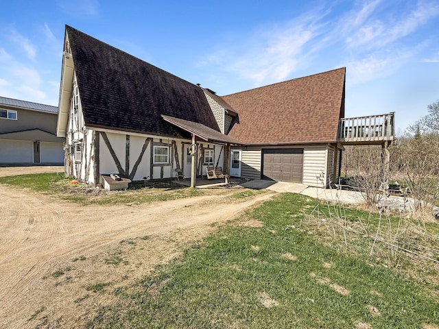 view of front of home featuring dirt driveway, an attached garage, roof with shingles, stucco siding, and a front yard