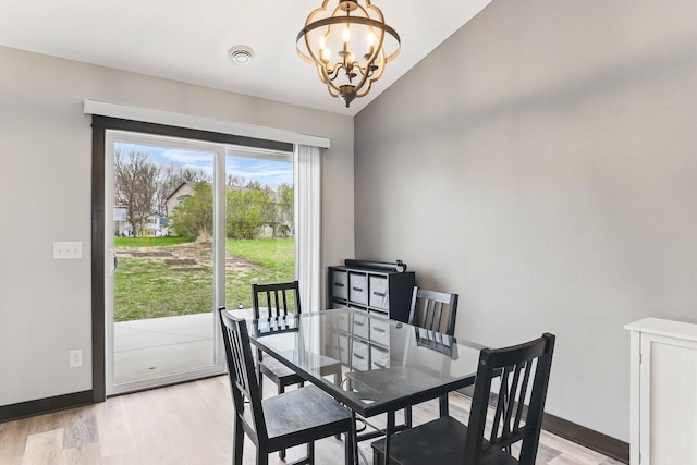 dining space featuring a chandelier, light wood finished floors, baseboards, and lofted ceiling