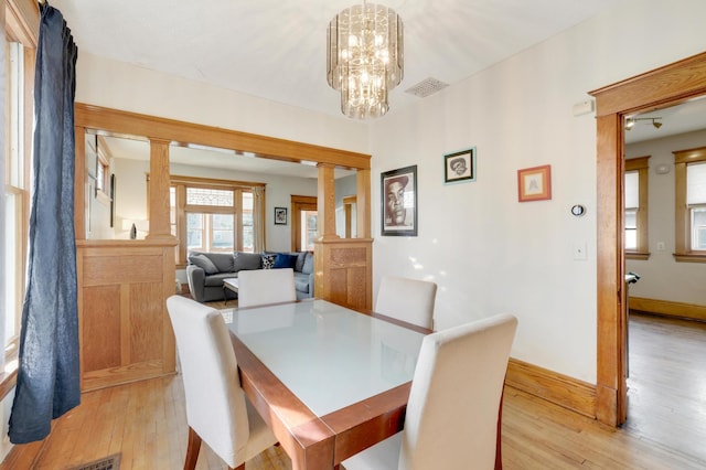 dining area featuring ornate columns, light wood-style floors, a chandelier, and baseboards