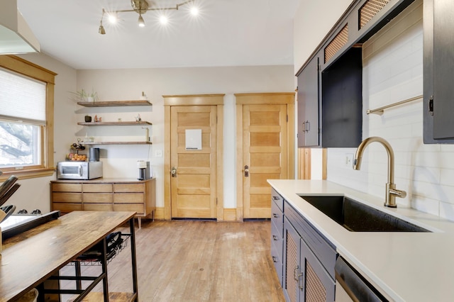kitchen featuring a sink, light wood-type flooring, light countertops, backsplash, and gray cabinetry