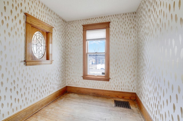 empty room featuring wallpapered walls, wood-type flooring, and baseboards