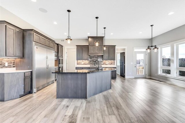 kitchen featuring stainless steel built in refrigerator, backsplash, light wood-type flooring, recessed lighting, and a sink