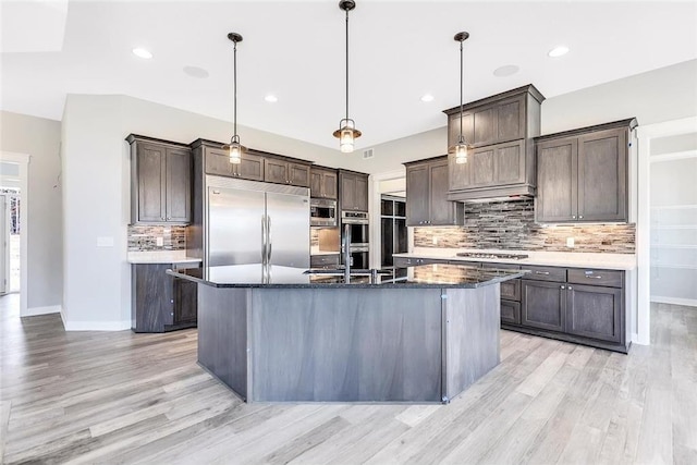 kitchen with built in appliances, a sink, dark brown cabinets, light wood finished floors, and decorative backsplash