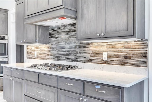 kitchen featuring stainless steel appliances, gray cabinetry, decorative backsplash, and light stone counters