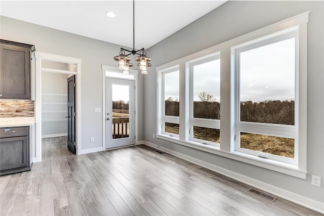 unfurnished dining area with a chandelier, light wood finished floors, and baseboards