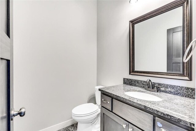half bath with baseboards, vanity, toilet, and marble look tiles