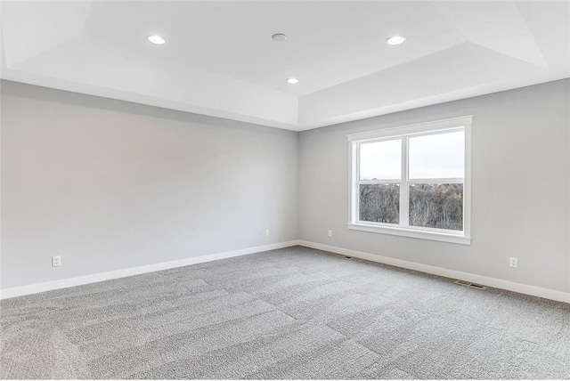 empty room with a raised ceiling, carpet flooring, recessed lighting, and baseboards