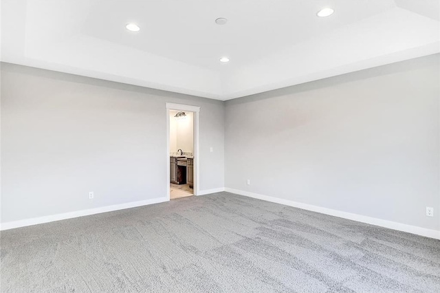 spare room featuring a raised ceiling, light carpet, recessed lighting, and baseboards