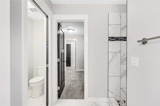 bathroom featuring toilet, marble look tile flooring, baseboards, and a shower