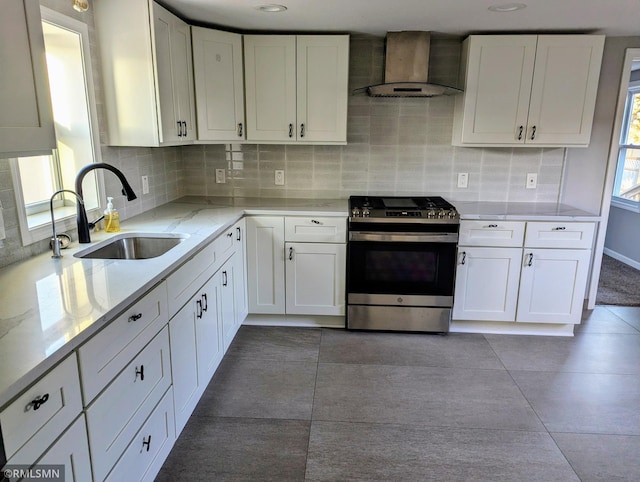 kitchen with stainless steel gas range, wall chimney exhaust hood, a sink, white cabinetry, and tasteful backsplash