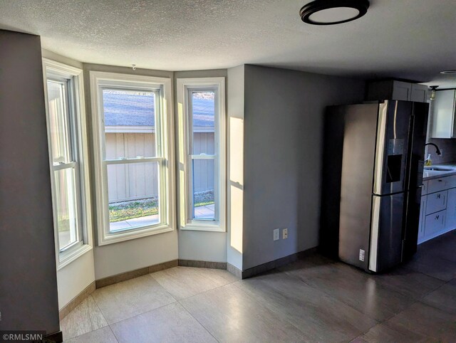 unfurnished dining area featuring a sink, healthy amount of natural light, a textured ceiling, baseboards, and tile patterned flooring