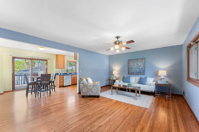 living area featuring light wood-style flooring, a ceiling fan, and baseboards