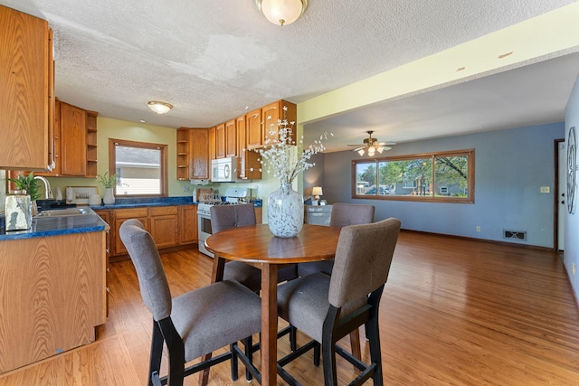 dining space with light wood-type flooring, a textured ceiling, a ceiling fan, and baseboards