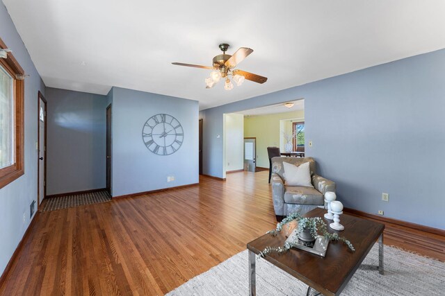 living area with a ceiling fan, wood finished floors, and baseboards