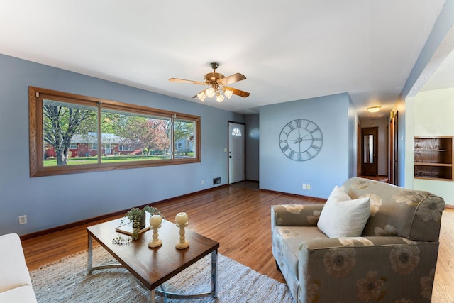 living room featuring ceiling fan, baseboards, and wood finished floors