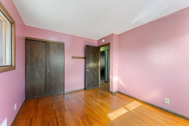 unfurnished bedroom with wood finished floors, baseboards, and a closet