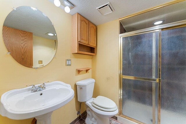 full bathroom featuring a sink, a shower stall, toilet, a textured ceiling, and baseboards