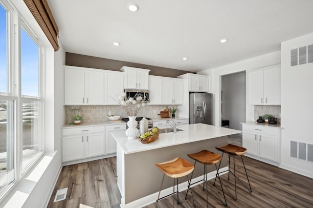 kitchen featuring stainless steel appliances, decorative backsplash, wood finished floors, a kitchen island with sink, and light countertops