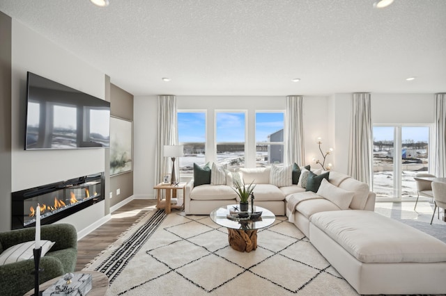 living area with a glass covered fireplace, recessed lighting, wood finished floors, a textured ceiling, and baseboards