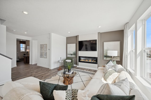 living area with wood finished floors, a glass covered fireplace, recessed lighting, and baseboards