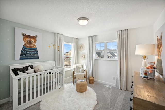 bedroom with carpet, baseboards, a textured ceiling, and a crib