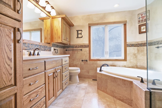 full bath with toilet, tile patterned floors, a bath, vanity, and tile walls