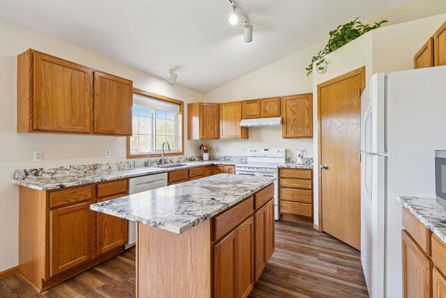 kitchen featuring white appliances, under cabinet range hood, a sink, lofted ceiling, and dark wood-style floors