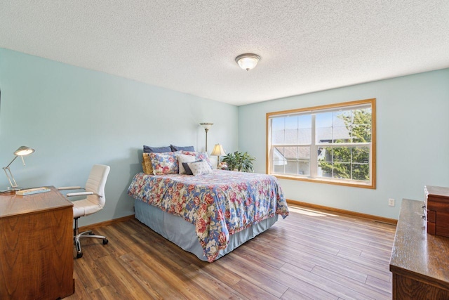 bedroom with baseboards, wood finished floors, and a textured ceiling
