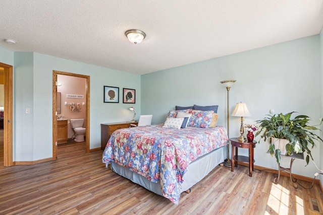 bedroom with wood finished floors, baseboards, a textured ceiling, and connected bathroom