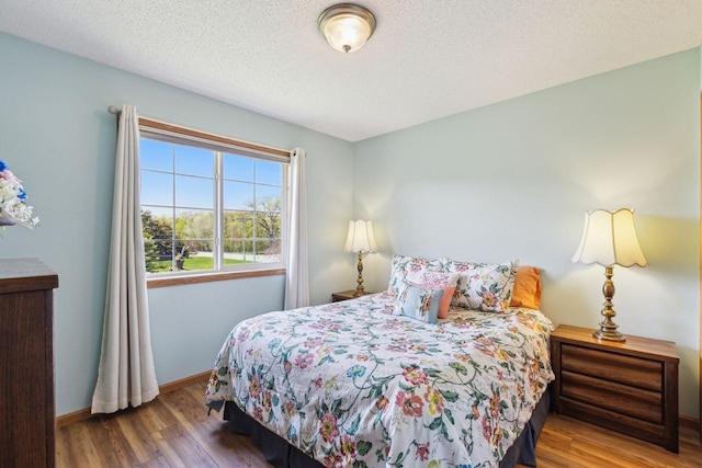 bedroom with wood finished floors, baseboards, and a textured ceiling